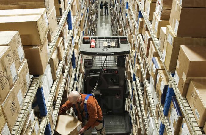 Looking down on an employee picking a box out of a rack, while standing on a motorized stock picker in a distribution warehouse.